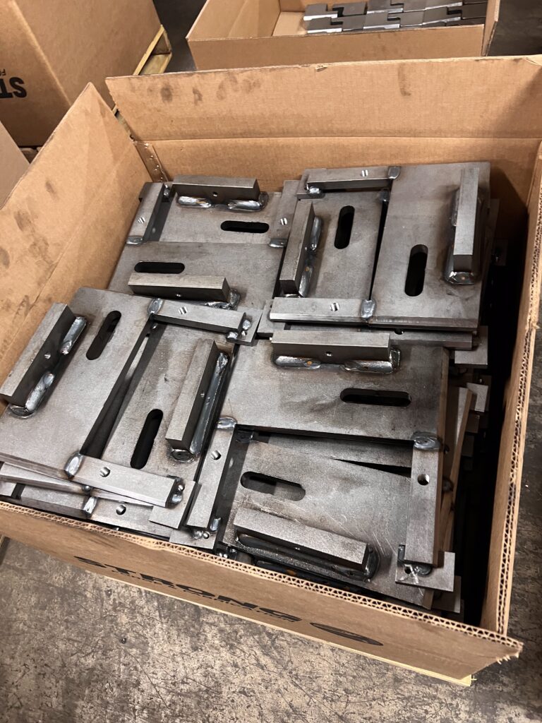 Stack of fabricated steel mounting plates with welded brackets and slotted holes