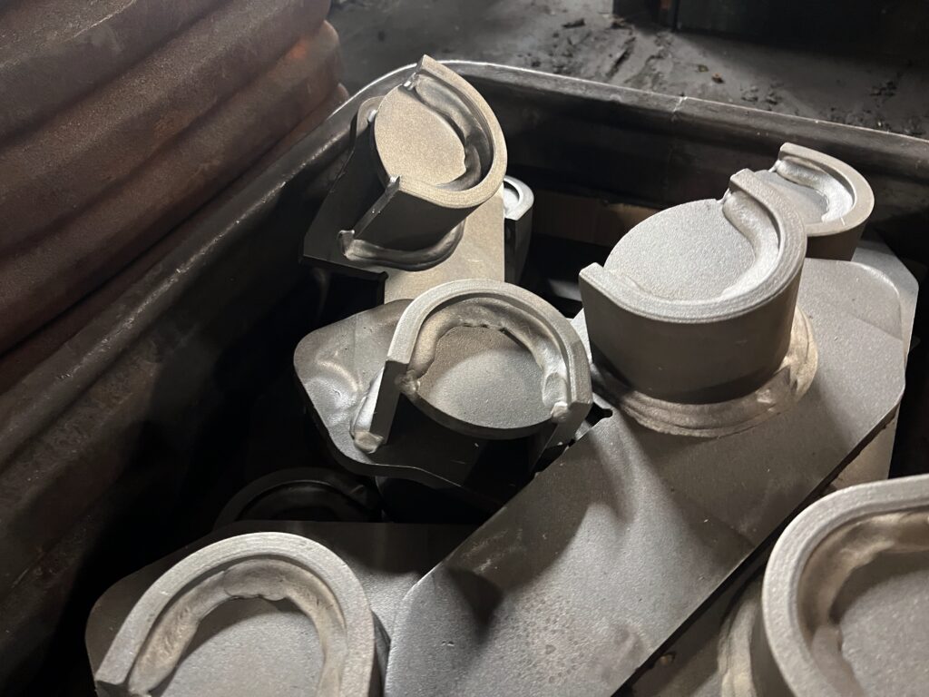 Cluster of precision-fabricated metal components with circular openings and welded features, finished with a textured coating and grouped together in an industrial bin.
